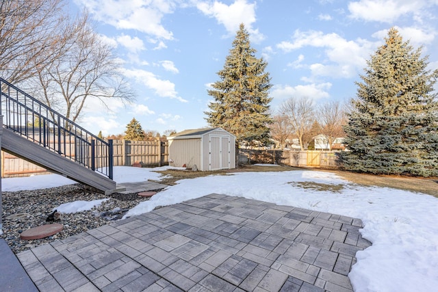 snow covered patio with a fenced backyard, a storage unit, and an outdoor structure