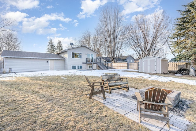 snow covered house with fence, stairs, an outdoor structure, a storage unit, and a patio area