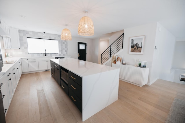 kitchen featuring a kitchen island, dark cabinets, a sink, white cabinetry, and light wood-type flooring