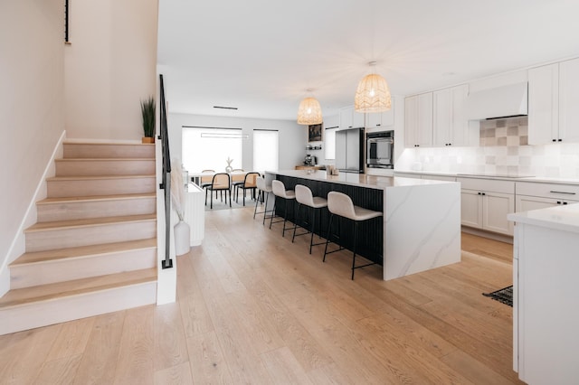 kitchen with premium range hood, decorative backsplash, light wood-style flooring, a kitchen breakfast bar, and white cabinetry