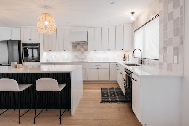 kitchen featuring a breakfast bar area, light wood-type flooring, white cabinetry, fridge, and a sink