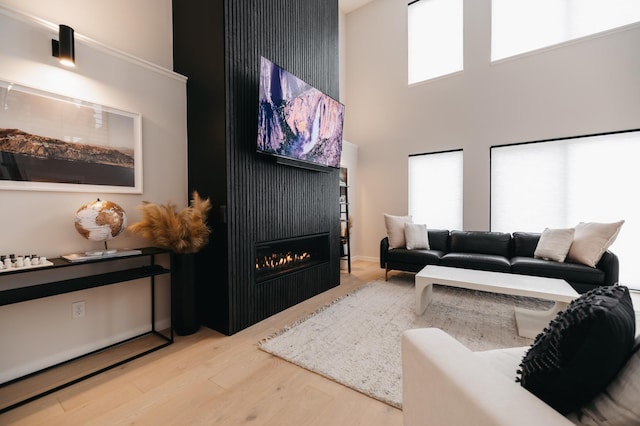 living room featuring a wealth of natural light, wood finished floors, a high ceiling, and a warm lit fireplace