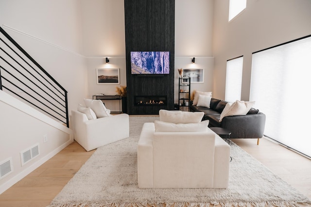 living area featuring visible vents, a large fireplace, stairway, a towering ceiling, and wood finished floors