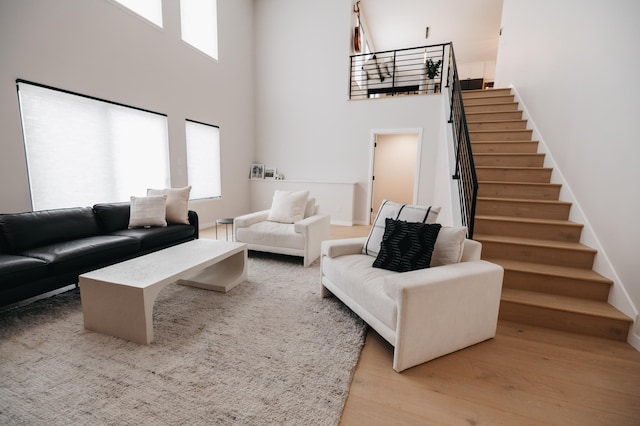 living room featuring baseboards, stairs, light wood-type flooring, and a towering ceiling