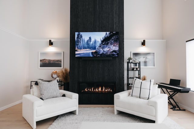 living area with a high ceiling, wood finished floors, baseboards, and a lit fireplace