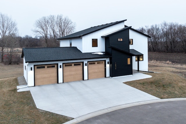 modern inspired farmhouse featuring concrete driveway, an attached garage, a front yard, and a shingled roof