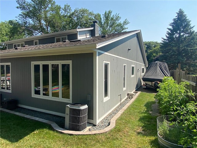 view of property exterior with central AC unit, fence, a yard, a shingled roof, and a chimney