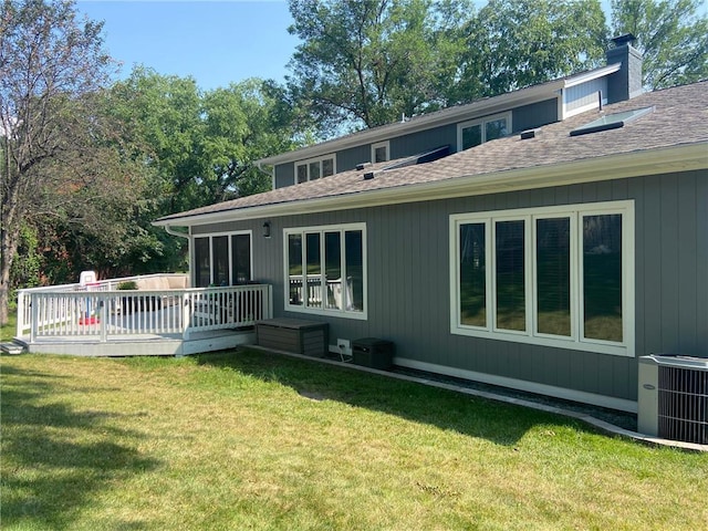 back of property featuring central AC unit, a yard, a chimney, a shingled roof, and a deck