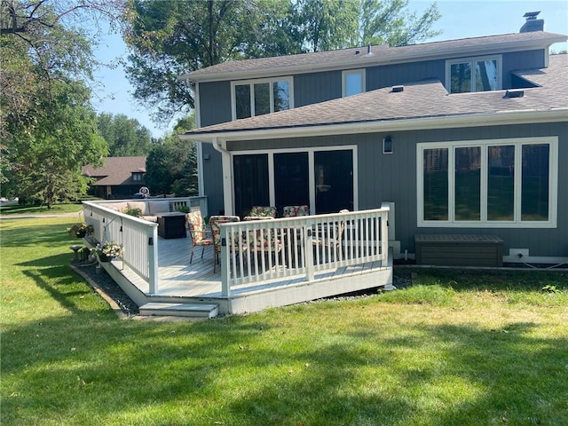 rear view of house with a deck, a yard, roof with shingles, and a chimney