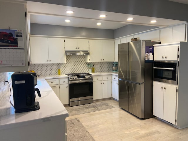 kitchen featuring light wood-style flooring, light countertops, under cabinet range hood, appliances with stainless steel finishes, and backsplash