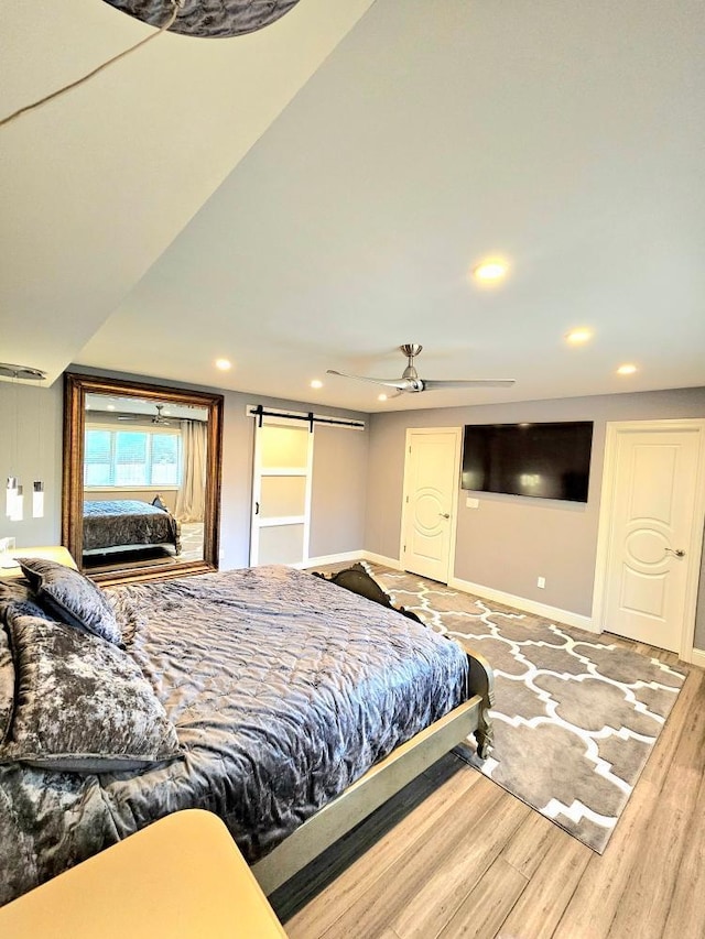 bedroom with recessed lighting, baseboards, a barn door, and wood finished floors