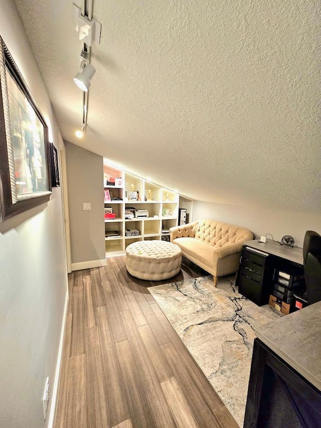 living area with lofted ceiling, track lighting, a textured ceiling, wood finished floors, and baseboards