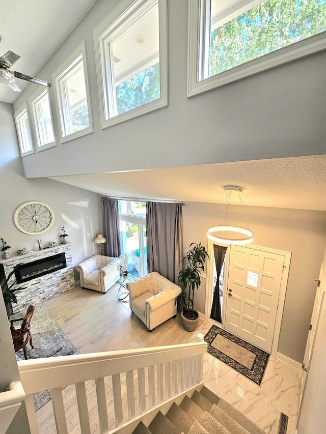 entryway with a stone fireplace, baseboards, marble finish floor, and a towering ceiling