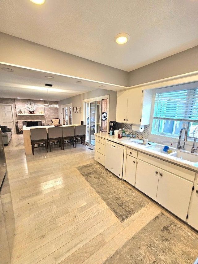 kitchen with dishwasher, light wood-type flooring, light countertops, white cabinetry, and a sink