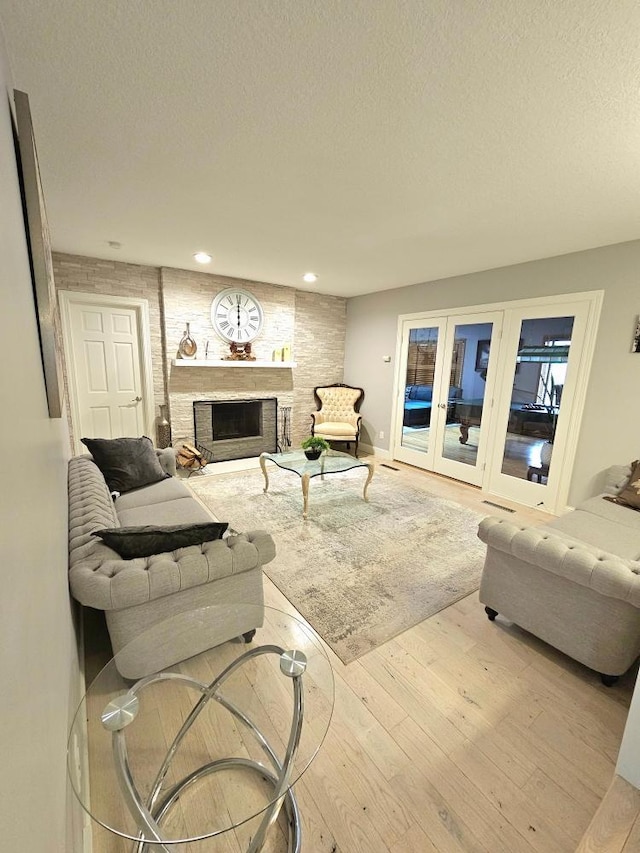 living room with a textured ceiling, wood finished floors, recessed lighting, french doors, and a fireplace