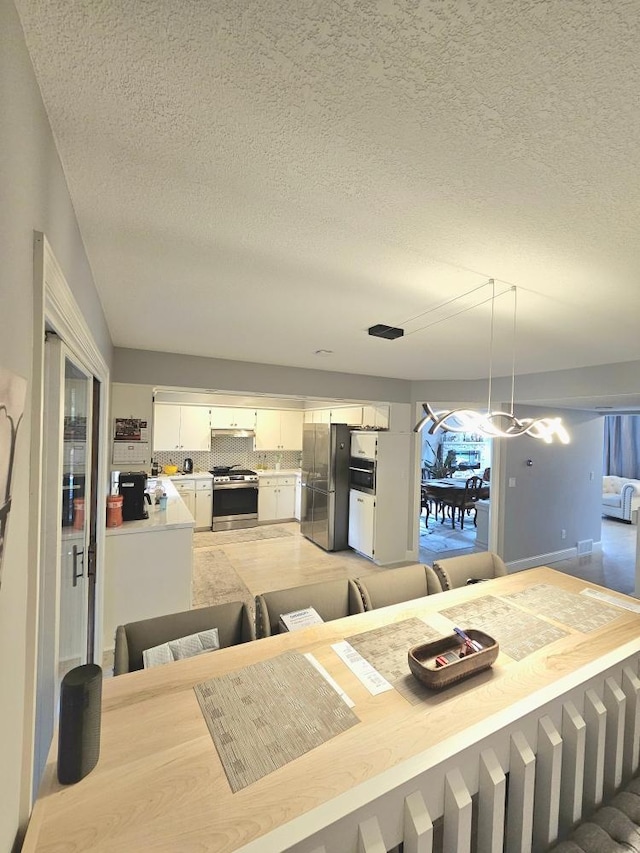 kitchen featuring under cabinet range hood, backsplash, stainless steel appliances, white cabinets, and light countertops