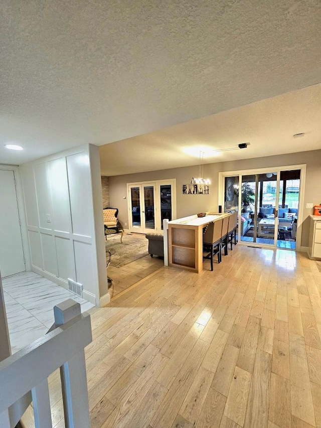 living room with visible vents, light wood finished floors, french doors, a textured ceiling, and a chandelier