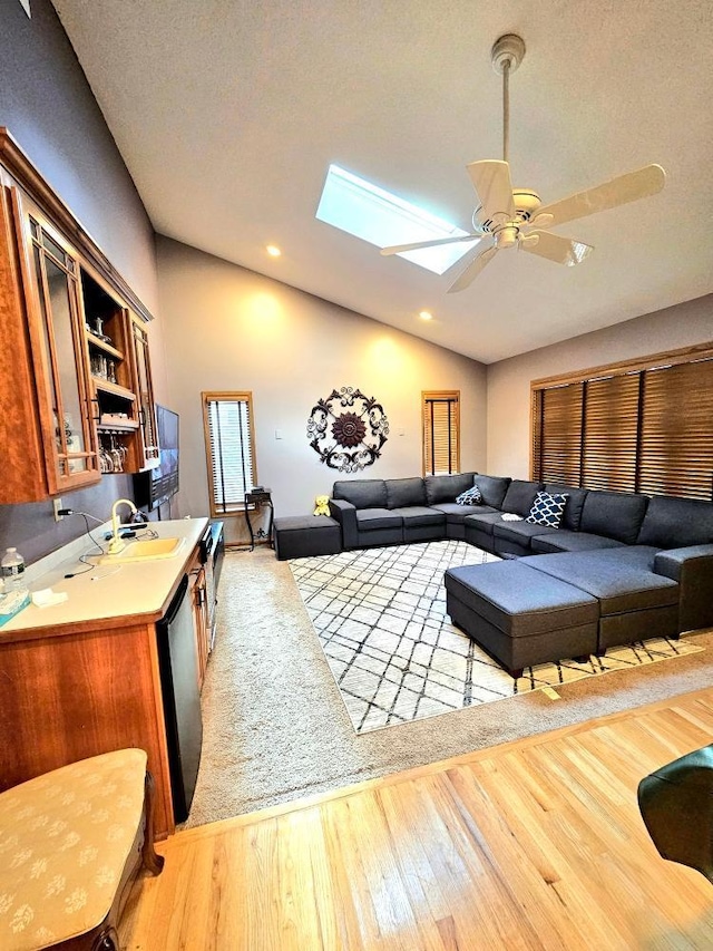 living room featuring vaulted ceiling with skylight, recessed lighting, light wood-style floors, and ceiling fan