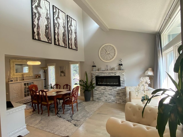 dining space featuring wood finished floors, high vaulted ceiling, beam ceiling, a fireplace, and a textured ceiling