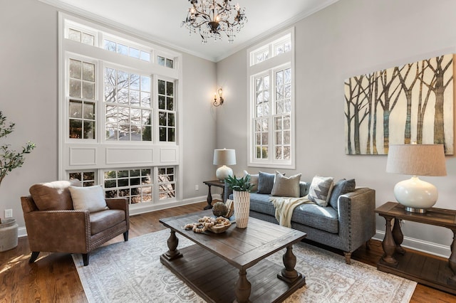 living area featuring baseboards, wood finished floors, an inviting chandelier, and ornamental molding