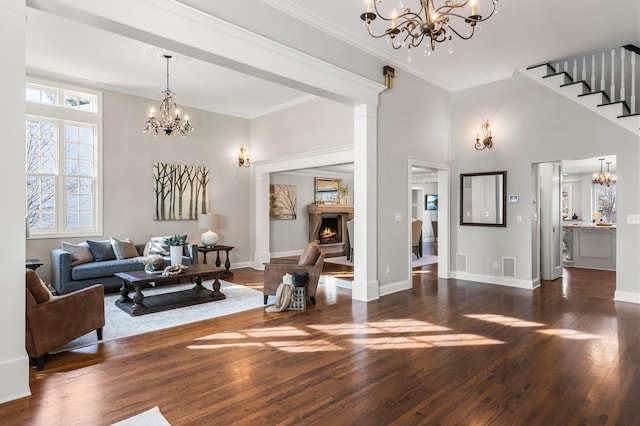 living area with wood finished floors, a warm lit fireplace, a chandelier, and ornamental molding