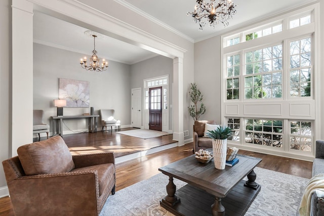 living area with a notable chandelier, ornamental molding, baseboards, and wood finished floors