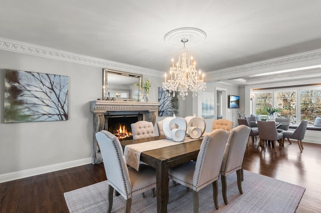 dining room featuring a notable chandelier, a warm lit fireplace, wood finished floors, crown molding, and baseboards