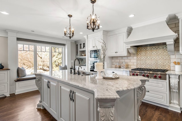 kitchen with a notable chandelier, a kitchen island with sink, a sink, appliances with stainless steel finishes, and custom exhaust hood