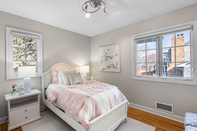 bedroom with visible vents, multiple windows, baseboards, and wood finished floors