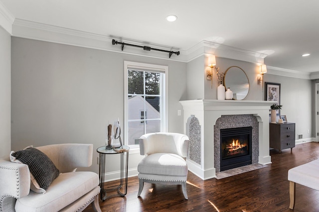 living area with baseboards, a fireplace with flush hearth, wood finished floors, and crown molding