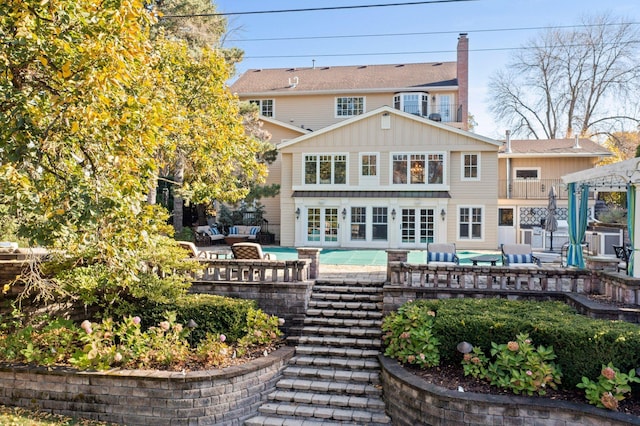 back of house featuring an outdoor living space, a fenced in pool, board and batten siding, and a chimney