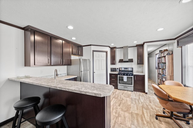 kitchen with a peninsula, light countertops, dark brown cabinets, appliances with stainless steel finishes, and wall chimney exhaust hood