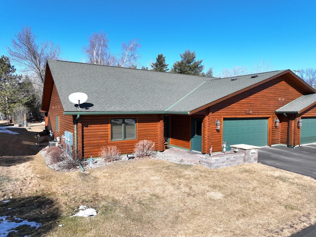 cabin with a garage, log exterior, driveway, and roof with shingles