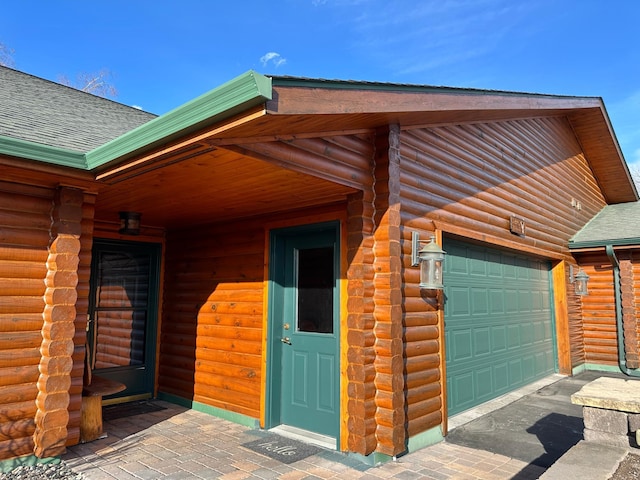 view of exterior entry with log siding and a shingled roof