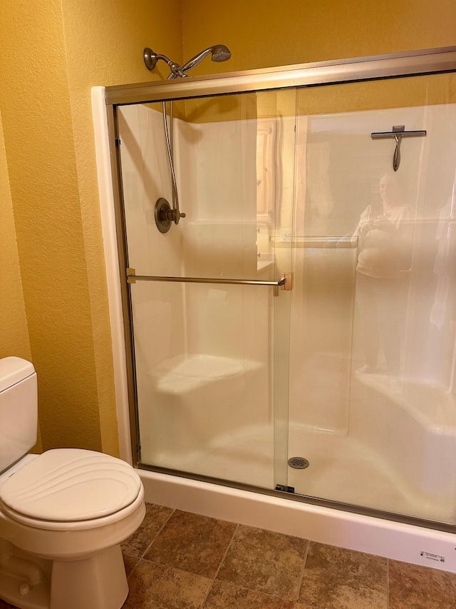 bathroom with toilet, a textured wall, and a stall shower