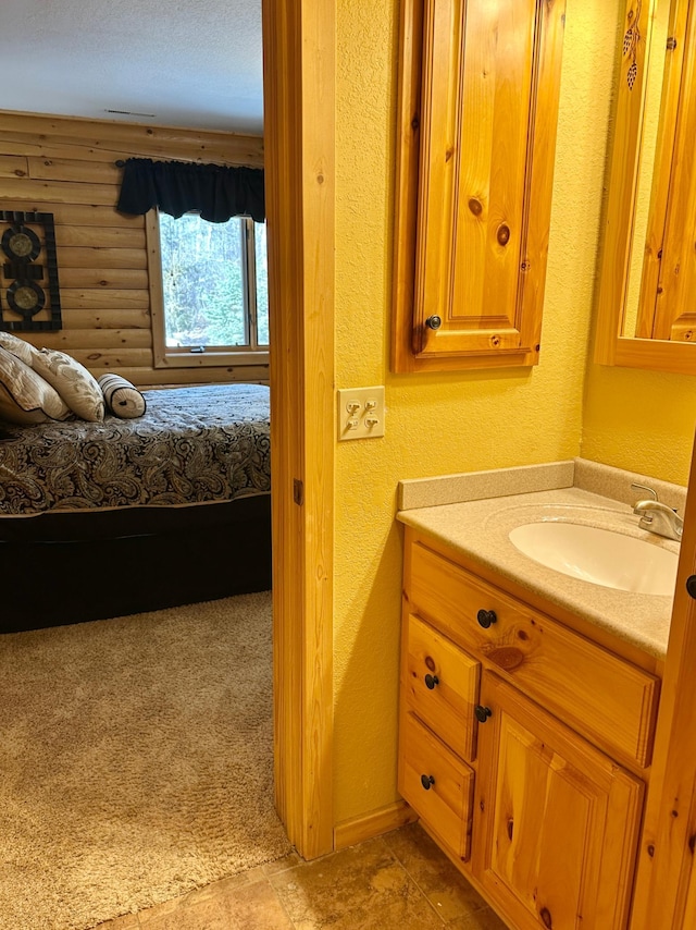 bathroom featuring connected bathroom, log walls, vanity, and a textured wall