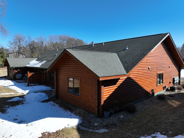 view of snowy exterior featuring cooling unit and a shingled roof