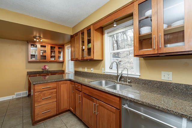 kitchen featuring brown cabinetry, visible vents, a sink, glass insert cabinets, and dishwasher