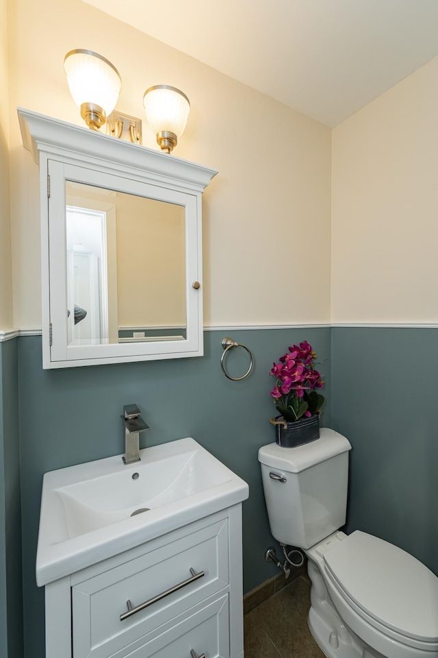 half bath with tile patterned floors, baseboards, toilet, and vanity