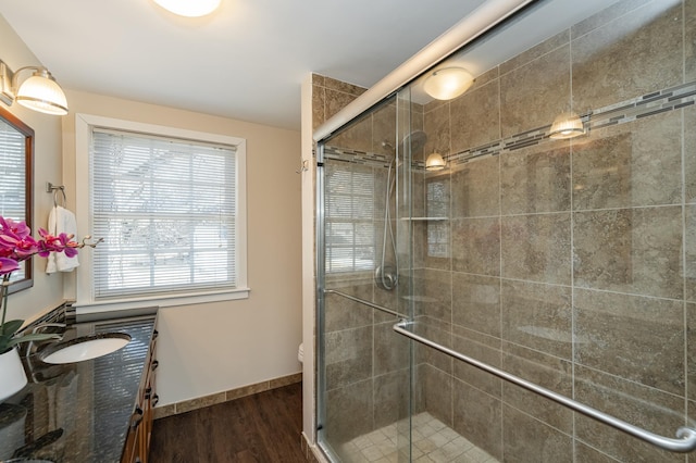 full bathroom with a stall shower, vanity, baseboards, and wood finished floors