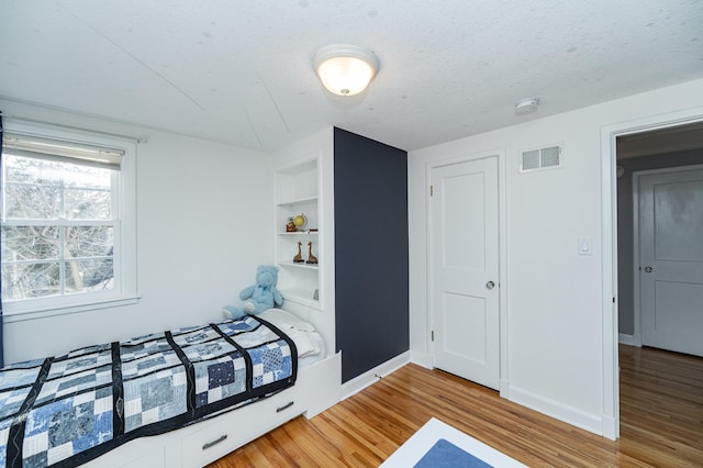 bedroom featuring visible vents, a textured ceiling, baseboards, and wood finished floors