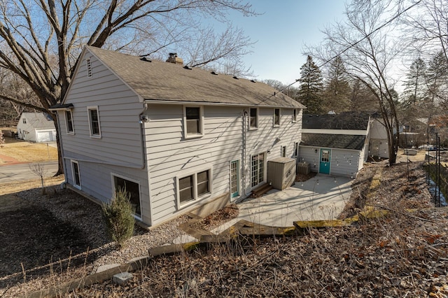 rear view of property with a shingled roof, a chimney, and a patio area