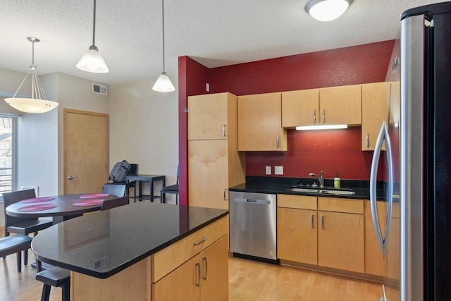 kitchen with visible vents, a sink, light wood-style floors, appliances with stainless steel finishes, and dark countertops