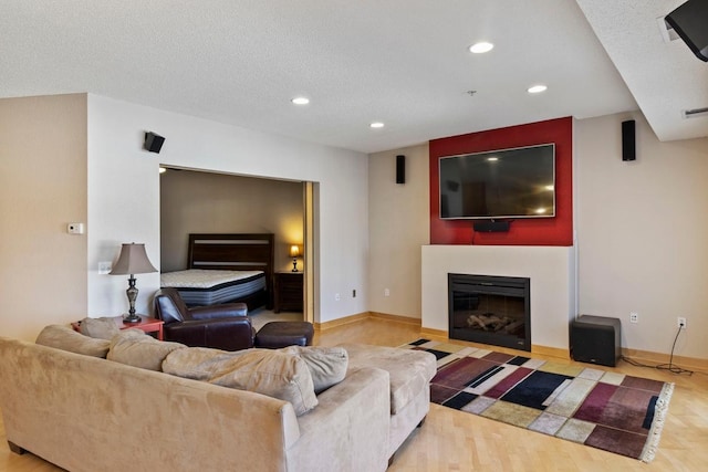 living area with baseboards, a fireplace with flush hearth, recessed lighting, wood finished floors, and a textured ceiling