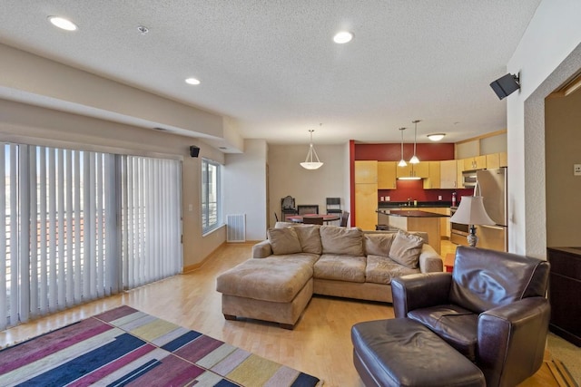 living room with recessed lighting, visible vents, light wood-style flooring, and a textured ceiling