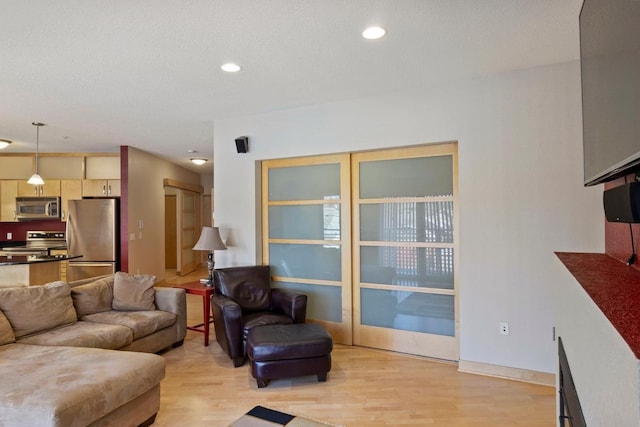 living room featuring recessed lighting, baseboards, light wood finished floors, and a textured ceiling