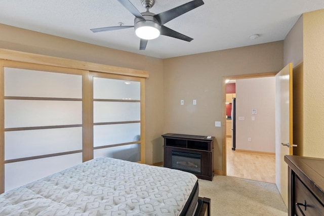 bedroom featuring a glass covered fireplace, light colored carpet, and a ceiling fan