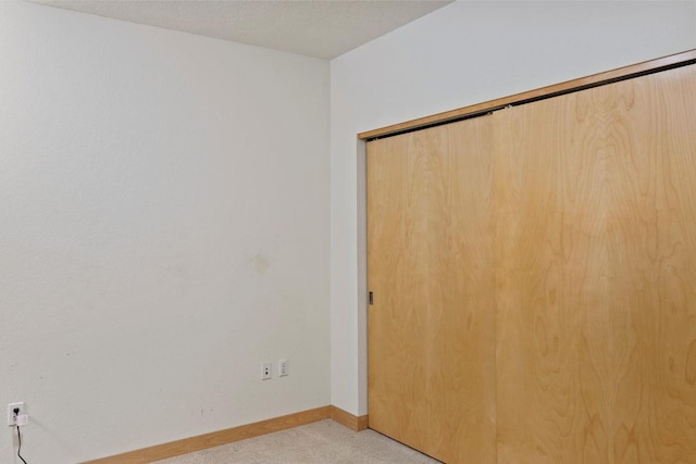 empty room with light carpet, a textured ceiling, and baseboards