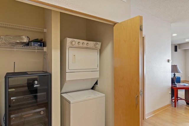 washroom with baseboards, wine cooler, laundry area, stacked washer and clothes dryer, and wood finished floors