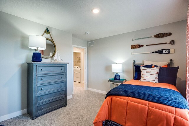 bedroom featuring visible vents, baseboards, light colored carpet, and washer / dryer